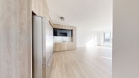 Located on the 15th floor at 33 8th Street in San Francisco's SoMa neighborhood, this single-floor residence showcases a clean, contemporary aesthetic throughout. The open-plan living and kitchen area is unified by light-toned hardwood flooring and crisp white walls, creating a bright and airy atmosphere. The kitchen is thoughtfully integrated into a warm wood-paneled enclosure, housing a stainless steel Bosch range, built-in microwave, and full-size refrigerator, complemented by white quartz countertops and a sleek tile backsplash. Dark upper cabinetry provides a refined contrast to the natural wood lower cabinets.

The living area benefits from generous floor-to-ceiling windows that frame sweeping views of the San Francisco skyline, flooding the space with abundant natural light. Bedroom spaces continue the minimalist palette, featuring the same light hardwood flooring, white walls, and large windows with city views and vertical panel detailing for added architectural interest.

The bathroom exhibits a spa-like quality, with a marble-tiled walk-in glass shower, light wood vanity with a dark countertop, large-format floor tiles, and expansive mirrors. Throughout the unit, the cohesive use of natural materials and a neutral color palette creates a calm, sophisticated urban living environment.