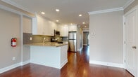 Located at 45 Cambridge Terrace, this single-floor residence offers a thoughtfully designed layout that balances functionality with modern finishes. Rich hardwood flooring runs consistently throughout the living areas and bedrooms, complemented by crisp white crown moulding and neutral-toned walls that create a clean, cohesive aesthetic.

The kitchen serves as a focal point of the space, featuring white shaker-style cabinetry, light granite countertops, and a sage-green subway tile backsplash. A peninsula with beadboard detailing provides additional workspace and casual seating. Stainless steel appliances, including a gas range, over-range microwave, refrigerator, and dishwasher, complete the well-equipped cooking area. Recessed lighting illuminates the kitchen and adjoining living space effectively.

The open living area offers generous proportions, with natural light filtering in through a sliding glass door fitted with vertical blinds and a ceiling fan overhead. Additional rooms feature windows with blinds, crown moulding, and the same warm hardwood flooring.

The bathroom is finished with large-format beige tiles on both the floor and tub surround, paired with a dark-cabinetry vanity and brushed nickel fixtures, lending a clean and classic feel to the space.