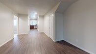 This single-floor unit offers a thoughtfully designed layout that balances comfort and functionality. The expansive living area is finished with rich, dark hardwood-style flooring and neutral gray walls, creating a clean and modern aesthetic. A sliding glass door floods the space with natural light and provides direct access to an outdoor patio area, offering pleasant views of surrounding greenery and a pergola structure.

The kitchen is well-equipped with dark wood cabinetry, stainless steel appliances including a refrigerator, electric range, microwave, and dishwasher, complemented by a tile backsplash and a window above the sink. A connecting hallway with the same hardwood-style flooring leads seamlessly between the living and private areas of the unit.

Two bedrooms are finished with plush wall-to-wall carpeting and feature windows with blinds that allow for natural light while maintaining privacy. Each room offers a calm, neutral palette well-suited for a variety of uses.

The unit includes two bathrooms. The primary bathroom features a dark wood vanity, wood-style flooring, and a glass-enclosed stand-up shower. The secondary bathroom includes a soaking tub with tiled surround and brushed nickel hardware. Together, these spaces provide a clean, functional, and comfortable living environment.