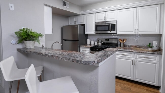 Whip up meals with ease in this stylish kitchen, complete with stainless steel appliances, white cabinetry, and a breakfast bar perfect for casual dining. - The Enclave at Huntington Woods