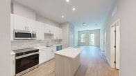 Unit 113 at 303 Lincoln St in Marlborough, MA is a well-appointed one-bedroom, one-bathroom residence designed with modern finishes throughout. Light wood-tone flooring runs consistently across the entire unit, creating a cohesive and clean aesthetic from room to room. The kitchen is a standout feature, offering white flat-panel cabinetry extending to the ceiling, a neutral tile backsplash, white quartz countertops, a central island for added prep space, and a full suite of stainless steel appliances including a range, microwave, dishwasher, and refrigerator. The adjacent dining area flows naturally from the kitchen, providing a functional and open layout. The living and dining spaces benefit from large windows that invite abundant natural light and offer views of the surrounding courtyard and greenery. The bedroom is a comfortable size, featuring its own dedicated closet with built-in shelving and two doors for easy access. The bathroom is finished in a crisp, modern style with light wood flooring, clean white walls, a glass-enclosed walk-in shower, and a vanity with contemporary hardware. The overall ambiance of the unit is bright, clean, and move-in ready, reflecting a contemporary design sensibility throughout.