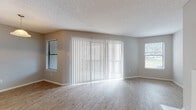 This two-floor residence offers a thoughtfully arranged layout with a blend of practical finishes and comfortable living spaces throughout. The main living area is notably bright, featuring light wood-look flooring, neutral gray walls, and a textured ceiling. Large sliding glass doors dressed with vertical blinds allow an abundance of natural light to fill the room, complemented by additional windows on adjacent walls. A pass-through window connects the living area to the kitchen, creating an open, communicative flow between spaces. The kitchen is outfitted with white cabinetry, granite-look countertops, a stainless electric range, a built-in microwave, and a stylish gray subway tile backsplash that adds a modern touch. The bedrooms feature plush carpeting, ceiling fans with light fixtures, and windows with horizontal blinds. Closet space is provided via sliding panel doors with built-in hanging rods. The bathrooms maintain a clean, functional aesthetic with wood-look tile flooring, white tub-shower surrounds equipped with built-in shelving niches, and simple, crisp fixtures. Overall, the space presents a neutral, move-in-ready environment with consistent finishes across both floors.