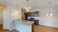 Located at 1910 Stonehenge Dr in Greenville, NC, this single-story residence offers a well-designed layout with modern finishes throughout. The kitchen serves as a central highlight, featuring dark espresso cabinetry, granite countertops, a subway tile backsplash, and a full suite of stainless steel appliances including a refrigerator, electric range, and built-in microwave. A peninsula with an undermount sink and pendant lighting above provides both additional workspace and a casual dining area. Light wood-style flooring runs throughout the main living areas, lending a clean, cohesive aesthetic.

The living area is bright and open, with a ceiling fan and sliding glass doors that lead to a private balcony with outdoor views. A dedicated hallway connects the living space to the bedrooms, each of which features plush carpeting, ceiling fans, and windows that allow ample natural light. The bathrooms are outfitted with dark vanity cabinetry, granite countertops, framed mirrors, and tub/shower combinations with wood-style flooring. A dedicated laundry room accommodates a full-size washer and dryer and includes overhead wire shelving for additional storage.
