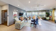 Located at 2540 Bluffs View Dr in Raleigh, NC, this well-appointed single-floor space offers a thoughtfully designed open layout encompassing a living room, dining room, and kitchen. The kitchen stands out with its rich, dark wood cabinetry, gray laminate countertops, and vibrant lime-green walls that create an energizing atmosphere. It features a full suite of appliances including a range, dishwasher, and double sink, complemented by woven pendant lighting that adds a warm, inviting touch. The open pass-through connects seamlessly to the dining and living areas, promoting a flowing, communal feel. The living room is generously proportioned, filled with natural light streaming through multiple large windows dressed with wood-toned blinds and decorative valances. A ceiling fan, recessed lighting, and an entertainment console anchor the space, which is furnished with colorful, eclectic seating arrangements set atop patterned area rugs over light hardwood-style flooring. The dining area offers flexible seating with both café-style bar stools and standard dining tables surrounded by patterned green chairs. Artwork and lush indoor plants are thoughtfully placed throughout, adding color and life to the neutral gray and green palette. The overall ambiance is bright, welcoming, and well-suited for social gatherings.