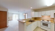 This single-floor residence is designed with a practical, open layout that promotes ease of movement throughout. The kitchen is well-equipped with white cabinetry, a double-basin sink, a white electric range, refrigerator, and dishwasher. Light-toned countertops provide ample workspace, and tile flooring runs throughout the cooking area. A peninsula with a breakfast bar connects the kitchen to the open living space, where soft carpeting and a pendant light fixture create a welcoming atmosphere. A sliding glass door in the living area allows natural light to flow in and provides access to an outdoor space with views of surrounding greenery.

The bedrooms are carpeted and feature neutral walls, baseboard heating, and windows that invite natural light. One bedroom includes a ceiling fan with lighting. Warm wood-toned baseboards and door trim add continuity throughout. Two bathrooms serve the unit: one with a shower/tub combination equipped with a safety grab bar and patterned tile flooring, and a second larger bathroom with a white vanity and spacious layout, also featuring patterned tile flooring and an accessibility grab bar. The overall design is clean and functional.