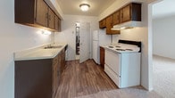 This single-floor unit offers a straightforward, functional layout across several distinct areas. The living room is generously proportioned, featuring neutral wall-to-wall carpeting and a sliding glass door fitted with vertical blinds that allows natural light to fill the space and provides access to an outdoor area. A pass-through opening connects the living room to an adjacent area, adding an element of openness to the layout.

The kitchen is designed in a galley configuration, featuring dark wood cabinetry lining both walls, light countertops, and wood-look plank flooring. White appliances, including a range and refrigerator, are complemented by an under-cabinet range hood. A single-basin sink sits along one wall, and a door leads to an adjacent space, enhancing the kitchen's connectivity within the unit.

The bedrooms continue the neutral carpeting and white walls, each with ample wall space and windows dressed with vertical blinds for light control and privacy. The bathroom features tile flooring, a dark wood vanity with a single-basin sink, light countertops, and dual mirrors above. Flush-mount lighting throughout the unit provides consistent, practical illumination across all rooms.