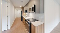 This 810-square-foot, one-bedroom, one-bathroom apartment at 16855 Redmond Way, Unit 216, offers a clean, modern aesthetic throughout. Light-toned luxury vinyl plank flooring flows seamlessly across all rooms, lending warmth and cohesion to the single-level layout. The galley-style kitchen features two-tone cabinetry — warm wood lower cabinets paired with matte gray uppers — white quartz countertops, a white subway tile backsplash, stainless steel appliances including a built-in microwave, dishwasher, and refrigerator, plus a black matte faucet at the undermount sink. The open living area is bathed in natural light from large windows and a sliding glass door leading to a private balcony. A wall-mounted mini-split unit provides climate control. The spacious 240-square-foot primary bedroom also features a sliding glass door to the balcony and a dedicated walk-in closet with double hanging rods and shelving. The full bathroom includes a dual-sink vanity with warm wood cabinetry, backlit LED mirrors, a glass-enclosed shower, and wood-look flooring. An in-unit laundry area completes this well-appointed apartment.