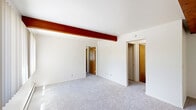 Located at 144 Highland Ave in East Lansing, MI, this single-floor unit offers three bedrooms and one bathroom across a compact, efficiently laid-out floor plan. A defining architectural detail throughout the space is the series of rich, dark wood beams that run across the ceilings, adding warmth and character to the otherwise neutral, white-walled interiors. Soft carpeting covers the floors of the living room and all three bedrooms, while the kitchen and bathroom feature hard surface flooring.

The living room is well-lit by large windows with vertical blinds that allow ample natural light, and baseboard heating runs along the walls for comfort. Each bedroom continues the beamed ceiling aesthetic and includes windows for natural light; the primary bedroom features a spacious sliding-door closet, while additional bedrooms offer their own closet storage and wall-unit air conditioning.

The galley-style kitchen is equipped with warm wood cabinetry, a white electric range, refrigerator, and a sink with counter space on both sides, topped with overhead cabinets for generous storage. The bathroom includes a full tub-shower combination with white tile surround and wood-look flooring, completing this practical and characterful East Lansing residence.