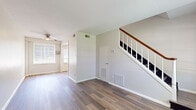 This upgraded two-story residence in Memphis, TN offers a well-designed layout spread across two floors. The main level features an open living room with hardwood-style flooring, a ceiling fan, and a large window fitted with blinds that allows abundant natural light to fill the space. A classic staircase with a wood handrail and white balusters connects both floors. The upgraded kitchen is a standout highlight, boasting white shaker cabinetry, subway tile backsplash, stone-look countertops, stainless steel appliances including a gas range and refrigerator, and recessed lighting. Upstairs, two bedrooms offer hardwood-style flooring and generous closet space, with the primary bedroom providing ample room for comfortable living. The bedrooms are connected via a hallway with convenient wall sconces. The full bathroom features a classic tiled design with bold navy and white tile accents, a soaking tub with shower, a white vanity, and a privacy window. Neutral gray walls and consistent flooring throughout the home create a cohesive, modern aesthetic that is both clean and functional.