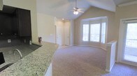 This single-floor residence offers a well-designed open layout that seamlessly connects the kitchen and living areas. The living room is defined by striking vaulted ceilings fitted with a ceiling fan, creating a sense of spaciousness and airflow throughout the space. Soft, neutral-toned carpeting covers the living area floor, lending warmth and comfort underfoot.

A prominent bay window arrangement floods the living space with generous natural light, offering a bright and welcoming atmosphere. The arched architectural detailing between spaces adds a refined touch to the overall design.

The kitchen features a raised bar counter finished with elegant granite countertops, providing both a functional workspace and a natural dividing element between the kitchen and the main living area. The tiled backsplash behind the counter adds a subtle decorative accent.

The entryway includes a closet with a clean white paneled door, offering convenient storage. Neutral-toned walls throughout the space contribute to a cohesive, understated aesthetic that pairs well with a variety of furnishing styles. Overall, the space combines practical design with architectural character, making it a comfortable and inviting single-floor home.