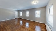 Located at 2 Rowe Pl in Bloomfield, NJ, this single-floor unit presents a clean, straightforward layout designed for practical everyday living. The space is finished with warm-toned hardwood flooring throughout the main living and bedroom areas, complemented by neutral gray walls and white trim that create a bright, cohesive aesthetic.

The spacious living area is a standout feature, offering generous square footage with multiple windows along one wall that allow ample natural light to fill the room. A wall-mounted radiator provides heating, and a flush ceiling fixture illuminates the space. The open feel of the living area flows naturally into the rest of the unit.

The kitchen is galley-style, lined with warm wood cabinetry on both upper and lower levels, white tile backsplash, and light countertops. It is equipped with a gas range, refrigerator, and a stainless sink beneath a window, with additional radiator heating and tile flooring. A utility panel is accessible in the adjacent hallway area.

The bedroom continues the hardwood flooring and neutral tones, with a window providing natural light and a ceiling light fixture overhead.

The bathroom features white ceramic tile flooring, a tiled tub-shower combination, a window for ventilation, and a wood-toned vanity, maintaining a clean and functional finish throughout.
