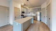Located at 4501 Town Center Blvd in Jeffersonville, Indiana, this one-bedroom, one-bathroom residence offers a thoughtfully designed single-floor layout. The kitchen serves as a central highlight, featuring gray shaker-style cabinetry, light quartz countertops, a large center island with pendant lighting, and a full suite of stainless steel appliances including a refrigerator, range, microwave, and dishwasher. Light wood-look flooring runs throughout the main living and kitchen areas, lending a clean, contemporary aesthetic. Panel-style doors with matte black hardware add a modern touch throughout the space. The bedroom is generously sized, finished with plush carpet, a ceiling fan with overhead lighting, and a window with blinds that invites natural light and outdoor views. A dedicated closet provides practical storage directly off the bedroom. The bathroom is well-appointed with dual under-mount sinks set into a quartz vanity top, gray cabinetry with black hardware, a large mirror with vanity lighting, and a full soaking tub with shower. Light wood-look flooring continues into the bathroom, tying the space together with a cohesive, modern finish throughout.