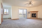 Located at 1300 Walnut St in Baraboo, Wisconsin, this well-appointed two-bedroom, two-bathroom single-floor residence offers a comfortable and functional layout. The spacious living room serves as the heart of the home, highlighted by a tile-surround corner fireplace with a warm wood mantel and a ceiling fan overhead. Plush carpeting runs throughout the living areas, and a sliding glass door opens to a private balcony, filling the room with natural light and offering pleasant outdoor views. The combined kitchen and dining area features warm oak cabinetry, ample counter space, tile flooring, and includes a dishwasher, electric range, and over-the-range microwave. Both bedrooms are carpeted and well-lit by windows with blinds, with the primary bedroom offering a generously sized layout and baseboard heating. The bathrooms include oak vanities, tile flooring, and a tub-shower combination. A dedicated laundry room adds everyday convenience, while five closets throughout the unit provide exceptional storage. Baseboard heating is present throughout the home, ensuring year-round comfort. The neutral color palette and warm wood accents create a cohesive and inviting atmosphere throughout this Baraboo residence.