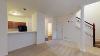 This two-story residential space offers a functional and well-organized layout designed for comfortable everyday living. The main level features an open living area finished with plush wall-to-wall carpeting, creating a warm and inviting atmosphere. A half-wall pass-through connects the living space to the kitchen, which is equipped with dark wood cabinetry and a countertop that doubles as a casual bar or dining surface. The kitchen also provides access to a full bathroom, conveniently positioned on the main floor and outfitted with hardwood-style flooring. The interior is finished with clean white walls and white panel doors throughout, contributing to a bright, cohesive aesthetic. Recessed lighting and standard overhead fixtures provide ample illumination across the main level. A staircase leads to the second floor, expanding the overall living footprint and offering additional private space. Floor vents indicate a central HVAC system for year-round climate control. The overall design balances practicality with a clean, neutral palette that provides a versatile canvas for personalization.