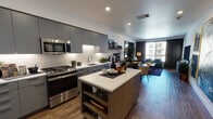 Located at 897 S Winchester Blvd in San Jose, California, this contemporary single-floor residence offers a thoughtfully designed open-concept layout with modern finishes throughout. The kitchen is a standout centerpiece, featuring floor-to-ceiling matte gray cabinetry, quartz countertops, stainless steel appliances including a gas range and built-in microwave, under-cabinet lighting, and a freestanding island with open shelving — ideal for both cooking and casual dining. The kitchen flows seamlessly into the living and dining areas, where warm hardwood-style flooring, large windows, and an abundance of natural light create an inviting, connected atmosphere. The living area is anchored by a large wall mirror that amplifies the sense of space, complemented by rich tones and contemporary furnishings. The bedroom offers a tranquil retreat with plush carpeting, a large window with outdoor views, and warm, layered lighting. The bathroom is finished with large-format tile in the shower/tub surround, tile flooring, a floating wood vanity, and a bold accent wall that adds a touch of personality. An in-unit washer and dryer complete this well-equipped residence, combining functional living with refined, urban style.