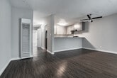 Located at 5200 S J St in Oxnard, California, this single-floor unit offers a practical and well-maintained layout designed for comfortable everyday living. Throughout the space, dark hardwood-style flooring provides a warm, cohesive aesthetic that ties the rooms together seamlessly.

The open living area is bright and inviting, featuring a ceiling fan with a light fixture and a textured ceiling. Natural light filters in through a sliding glass door with vertical blinds, enhancing the sense of openness. A secondary room with the same dark flooring and a louvered closet door offers flexible use as a bedroom or additional living space.

The kitchen is efficiently designed with gray cabinetry, speckled laminate countertops, and a black gas range with an overhead exhaust hood. A raised breakfast bar visually separates the kitchen from the living area while maintaining an open feel.

A hallway connects the main living spaces and includes wall-mounted lighting, a thermostat, and access to storage. The bathroom features wood-style flooring, a full tub-and-shower combination with white tile surround, and a toilet, providing all essential amenities in a clean, functional layout.

Overall, this unit presents a neutral color palette of whites and grays, updated finishes, and a straightforward floor plan suited to a variety of living arrangements.