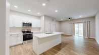 Located at 3108 Lockwood Ridge Rd. in Sarasota, Florida, this single-floor, one-bedroom, one-bathroom unit offers a well-designed layout with modern finishes throughout. Light wood-style flooring runs continuously across all rooms, creating a clean and cohesive aesthetic.

The open-concept kitchen and living area serves as the heart of the unit. The kitchen features crisp white shaker-style cabinetry, quartz countertops, a central island with a built-in sink, and a full suite of stainless steel appliances including a refrigerator, electric range, and over-the-range microwave. Recessed lighting and a ceiling fan illuminate the combined living space, which flows seamlessly from the kitchen.

The bedroom is a comfortable, well-proportioned room equipped with a ceiling fan, a large window that brings in natural light, a set of sliding double closet doors, and access to a private balcony through sliding glass doors — offering views of the surrounding greenery.

The bathroom is finished with a white shaker-style vanity, quartz countertop, a large mirror, and ample storage through multiple drawers and cabinet doors. Neutral, warm-toned walls throughout the unit contribute to a bright and inviting atmosphere. The overall design reflects a contemporary, move-in-ready aesthetic suited for comfortable single-floor living.