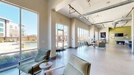 Located at 5437 Bowman Rd in Macon, Georgia, this single-floor clubhouse space offers a thoughtfully designed communal environment that blends modern industrial aesthetics with warm, inviting finishes. The open layout is anchored by soaring ceilings with exposed ductwork and sleek track lighting, lending an airy, loft-like character throughout.

The main living area is generously proportioned, featuring polished concrete floors that run seamlessly across the entire space. Expansive floor-to-ceiling windows and glass-panel walls flood the interior with abundant natural light while framing impressive views of an outdoor pool and courtyard area. Comfortable seating arrangements, including leather sofas and accent chairs, are thoughtfully positioned to take advantage of these views.

A standout feature is the large-scale abstract mural adorning one of the interior walls, adding a bold artistic focal point to the space. Adjacent to the lounge area is a recreation zone complete with a pool table and a bar-height counter with seating, backed by a kitchenette with dark cabinetry and a mounted television — ideal for social gatherings.

The entry area is equally impressive, with double glass doors, soaring vertical windows, and carefully curated décor including framed artwork and lush potted plants. The overall ambiance is modern, bright, and welcoming, making this a well-appointed communal destination.