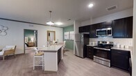 This single-floor residence is thoughtfully designed with an open-concept layout that connects the kitchen, dining, and living areas into one cohesive, functional space. The kitchen is a standout feature, outfitted with dark espresso cabinetry, granite countertops, a classic white subway tile backsplash, and a full suite of stainless steel appliances including a refrigerator, range, and over-the-range microwave. A central island with seating provides additional prep space and casual dining options, while a pendant light above adds a refined focal point. Light wood-style flooring runs throughout the main living areas, lending a clean, contemporary aesthetic.

The living room is inviting and well-proportioned, featuring a ceiling fan, crown molding, and large sliding glass doors that bring in natural light. A bold green accent wall adds visual depth and character to the space.

The bedrooms are carpeted for comfort and each feature ceiling fans and large sliding glass doors that provide outdoor access and ample natural light. Both bathrooms are finished consistently with the kitchen, incorporating dark cabinetry, granite countertops, and tub-shower combinations, creating a cohesive design language throughout the residence.