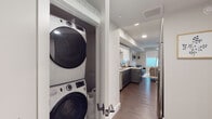 This thoughtfully designed single-floor residence offers a cohesive modern aesthetic throughout. The galley-style kitchen is a standout feature, showcasing a two-tone cabinet scheme with crisp white uppers and slate-gray lowers, complemented by quartz countertops, a marble-style tile backsplash, stainless steel appliances, and a matte black faucet. Recessed lighting and rich wood-look flooring tie the space together seamlessly as the kitchen flows into the living area.

The living room is bright and inviting, benefiting from a large window with a roller shade that fills the space with natural light. A ceiling fan adds comfort, while tasteful wall art and hanging greenery contribute to a relaxed, contemporary ambiance.

The bedroom features wood-look flooring, a walk-in closet with built-in shelving, and a window providing additional natural light. A creative neon wall accent adds a personalized, modern touch to the room.

Both bathrooms are finished with gray cabinetry, white countertops, light tile flooring, and matte black hardware, maintaining a consistent design language. Each bathroom includes a shower/tub combination and an overhead storage cabinet.

A dedicated in-unit laundry closet houses a full-sized stacked washer and dryer, offering exceptional convenience. The overall layout is efficient and well-organized, delivering a polished, move-in-ready living experience.