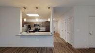 This two-story residence is designed with a modern, functional aesthetic that balances style and practicality throughout. The main level centers on an open-concept layout where the kitchen flows seamlessly into the living area. The kitchen is well-appointed with dark espresso cabinetry, granite countertops, a full suite of stainless steel appliances including a refrigerator, electric range, and built-in microwave, and a peninsula with an undermount sink and pendant lighting overhead. A skylight above the kitchen adds a notable source of natural illumination. The adjacent living area is generously proportioned, featuring wood-style plank flooring, a ceiling fan, and large windows alongside a door that provides outdoor access and fills the space with natural light.

The main level also includes a full bathroom with a tub/shower combination, dark wood cabinetry, granite countertops, and wood-style flooring. A hallway leads to a staircase connecting to the upper level, where the bedrooms are located. The bedrooms are carpeted and include ceiling fans, windows with exterior views, and access to walk-in closets outfitted with wire shelving systems. A second bathroom on the upper level features a double-sink vanity with granite countertops, matching espresso cabinetry, and additional storage above the toilet.
