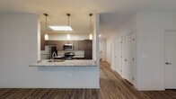 This two-story residence is designed with a modern, functional aesthetic that balances style and practicality throughout. The main level centers on an open-concept layout where the kitchen flows seamlessly into the living area. The kitchen is well-appointed with dark espresso cabinetry, granite countertops, a full suite of stainless steel appliances including a refrigerator, electric range, and built-in microwave, and a peninsula with an undermount sink and pendant lighting overhead. A skylight above the kitchen adds a notable source of natural illumination. The adjacent living area is generously proportioned, featuring wood-style plank flooring, a ceiling fan, and large windows alongside a door that provides outdoor access and fills the space with natural light.

The main level also includes a full bathroom with a tub/shower combination, dark wood cabinetry, granite countertops, and wood-style flooring. A hallway leads to a staircase connecting to the upper level, where the bedrooms are located. The bedrooms are carpeted and include ceiling fans, windows with exterior views, and access to walk-in closets outfitted with wire shelving systems. A second bathroom on the upper level features a double-sink vanity with granite countertops, matching espresso cabinetry, and additional storage above the toilet.