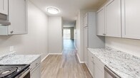Located at 2827 S Emporia St in Wichita, Kansas, this two-bedroom, two-bathroom residence is thoughtfully laid out across a single floor. The kitchen serves as a functional centerpiece, featuring gray shaker-style cabinetry, granite-look countertops, stainless steel appliances including a range and refrigerator, and light wood-look vinyl plank flooring. A hallway extends from the kitchen toward the living area, which benefits from a natural light source through sliding glass patio doors with vertical blinds. Both bedrooms are carpeted in a neutral tan tone and equipped with ceiling fans with light fixtures, creating a comfortable atmosphere. The primary bedroom offers a generous footprint, while the second bedroom includes a window with blinds, allowing in natural light. A dedicated closet provides additional storage. Both bathrooms feature wood-look vinyl flooring, granite-look vanity tops, white cabinetry, and a tub-shower combo with clean white surround panels. The overall color palette throughout the home is neutral and cohesive, with warm beige walls, white trim, and consistent finishes that lend the space a clean, move-in-ready appeal.