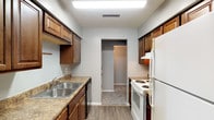 Located at 8 N Keene St in Columbia, Missouri, this single-floor unit offers a practical and comfortable layout designed to maximize everyday functionality. The galley-style kitchen is outfitted with rich wood cabinetry, granite-look countertops, a double stainless steel sink, a dishwasher, an electric range, and a full-size refrigerator. Wood-look vinyl flooring runs throughout the kitchen, lending a clean, durable finish to the space. The unit features multiple bedrooms, each finished with plush wall-to-wall carpeting and ceiling fans with light fixtures for year-round comfort. Natural light enters through windows dressed with horizontal blinds, and select rooms include sliding glass door access and built-in closets for added storage. One room also features a distinctive structural beam detail, adding architectural character to the space. The bathroom includes a wood-framed vanity mirror, a single-sink vanity with white countertop, a full tub-shower combination, and wood-look vinyl flooring that ties in cohesively with the rest of the unit. Neutral gray tones and white trim are used throughout, creating a clean and versatile backdrop adaptable to a variety of furnishing styles.