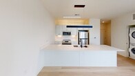 Located at 500 Maury St within The Track development in Richmond, VA, this two-bedroom unit offers a thoughtfully designed single-floor layout that maximizes both comfort and functionality. Throughout the space, light-toned hardwood flooring creates a clean, cohesive aesthetic that complements the bright white walls and modern finishes.

The kitchen serves as a central focal point, featuring a large peninsula with a white quartz countertop, undermount sink with a matte black faucet, white cabinetry, and stainless steel appliances including a refrigerator, range, and microwave. Sleek pendant lighting adds a contemporary accent above the peninsula.

The open living area flows naturally from the kitchen and is bathed in natural light through large windows and a sliding glass door that leads to a private outdoor balcony with wood decking and sweeping views of the Richmond skyline.

Both bedrooms are well-proportioned and bright, each equipped with a ceiling fan and oversized windows that frame elevated urban views. The spacious primary bedroom offers generous room to accommodate a full furniture suite. A connecting hallway provides convenient access between the bedrooms and the main living areas.

The overall ambiance is clean, modern, and light-filled, making this a well-appointed urban residence in a vibrant Richmond neighborhood.