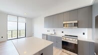 Located at 307 SW 5th St in Fort Lauderdale, FL, this modern 2-bedroom, 1-bathroom residence offers a well-designed layout with clean contemporary finishes throughout. Light-toned hardwood flooring flows seamlessly across every room, lending warmth and continuity to the space.

The kitchen serves as a standout feature, equipped with sleek flat-front cabinetry in a sophisticated grey finish, stainless steel appliances including a refrigerator, gas range, and microwave, all complemented by crisp white countertops. A central island provides additional prep and seating space, making the kitchen both functional and visually striking.

Both bedrooms are bright and airy, each featuring large floor-to-ceiling windows with roller shades that frame sweeping elevated views of the Fort Lauderdale cityscape and surrounding greenery. The clean white walls enhance the sense of openness in each room.

The bathroom is finished with large-format stone-look tile surrounding a soaking tub and shower combination, accented by matte black fixtures that add a refined, modern touch. A dedicated closet with built-in shelving and hanging rods offers organized storage. A clean hallway with matte black hardware connects the rooms, reinforcing the cohesive modern aesthetic found throughout this well-appointed residence.
