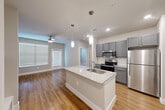 Located at 1720 Summit Crossing Lane in College Station, TX, this single-story 1-bedroom, 1-bathroom unit offers a thoughtfully designed layout with modern finishes throughout. The open-concept kitchen and living area serves as the heart of the space, anchored by a central island with a granite countertop, undermount sink, and stylish pendant lighting. The kitchen is outfitted with gray shaker-style cabinetry, a white subway tile backsplash, and a full suite of stainless steel appliances, including a refrigerator, electric range with microwave, and dishwasher. Warm hardwood-style flooring extends through the main living areas, complemented by recessed lighting and a ceiling fan. A dedicated pantry provides additional storage, while open shelving near the entryway adds functional character. The bedroom is a comfortable retreat featuring plush carpet, a ceiling fan, and a sizable window with blinds that allow natural light. It connects directly to the full bathroom, which features a granite-topped dual vanity with gray cabinetry, a large mirror, and a tiled shower. The in-unit laundry area houses a stacked Whirlpool washer and dryer alongside built-in shelving and a hanging rod, maximizing utility within a compact footprint.
