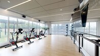 Located at 315 First Ave NE in Minneapolis, MN, this contemporary fitness facility offers a well-appointed, single-floor layout thoughtfully divided into distinct training zones. The space is designed with a clean, modern aesthetic, combining light hardwood flooring, polished concrete surfaces, and sleek linear ceiling lighting throughout.

The cycling and group fitness area serves as a bright, open centerpiece, featuring a row of Peloton spin bikes positioned in front of expansive floor-to-ceiling windows that flood the room with natural light and offer views of the surrounding neighborhood. A wall-mounted mirror, ballet barre, and large display screen make this zone equally suitable for group classes and individual workouts.

Adjacent to the cycling area, a dedicated functional training room features rubber flooring and a striking "Freedom Climber" climbing wall as its focal point — a circular wall-mounted climbing apparatus offering a unique and engaging challenge. This zone also houses a heavy punching bag, a RAX multi-functional training rig with pull-up bars and battle ropes, and weight storage, catering to strength and high-intensity training needs.

The space benefits from abundant natural light in the main areas, a sophisticated neutral color palette, and high-end equipment selections, creating a professional yet approachable environment suited for a wide range of fitness disciplines.