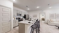 This thoughtfully designed 2-bedroom, 2-bathroom single-floor residence offers a clean, modern aesthetic throughout. The open-concept kitchen is a standout feature, showcasing gray shaker cabinets, granite countertops with a white-and-beige veining, a subway tile backsplash, and a full suite of stainless steel appliances. A large central island with bar seating provides additional prep space and casual dining. Light wood-look flooring runs throughout, lending the home a bright, cohesive feel. The adjacent dining area comfortably accommodates a small table, while the living room features elevated ceilings, recessed lighting, a ceiling fan, and windows that invite natural light. The primary bedroom is generously proportioned, complete with a ceiling fan, large windows, and its own en-suite bathroom fitted with granite vanity counters and a tub-shower combination. The second bedroom also receives ample natural light through its oversized window. Three dedicated closets — including a spacious walk-in with built-in shelving and hanging rods — provide excellent storage throughout. Both bathrooms echo the kitchen's refined finishes with matching gray cabinetry and granite surfaces, creating a consistent and polished design language across the entire home.