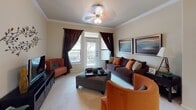 This single-story residence offers a thoughtfully designed layout with a variety of comfortable living spaces. The kitchen is equipped with warm medium-toned wood cabinetry, granite-style countertops, and black appliances including a range, built-in microwave, and dishwasher, all set atop tile flooring. The living room features crown molding, a ceiling fan, and a glass door opening to a private balcony, allowing natural light to fill the carpeted space. Adjacent to the living area, the dining room includes track lighting, crown molding, and decorative wall art, creating an intimate setting for gatherings. The primary bedroom benefits from a distinctive bay window that frames outdoor greenery, complemented by a ceiling fan and plush carpeting. A second bedroom also features a bay window and carpet flooring, while a third bedroom offers a bright window with decorative drapery. The primary bathroom presents a wide double-sink vanity with dark-framed mirrors, granite-style countertops, rich wood cabinetry, and a separate glass-enclosed shower. The secondary bathroom mirrors similar finishes with a single-sink vanity and a full tub-shower combination with tile surround. Neutral wall tones and consistent warm wood accents create a cohesive aesthetic throughout the home.