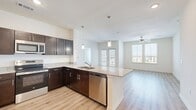 This well-appointed 4-bedroom, 2-bathroom single-floor residence offers a thoughtfully designed open-concept layout that maximizes functionality and comfort. The kitchen serves as the centerpiece of the common area, featuring rich dark-espresso cabinetry, granite countertops, stainless steel appliances including a refrigerator, microwave, dishwasher, and range, and a peninsula with an integrated sink and pendant lighting overhead. Light wood-style flooring flows seamlessly from the kitchen into the expansive living area, which is brightened by large windows and finished with a ceiling fan. The four bedrooms offer a mix of light wood-style flooring and plush carpeting, each equipped with ceiling fans and generously sized windows that invite natural light and exterior views. The two bathrooms are finished consistently with the rest of the home, showcasing dark vanity cabinetry with granite countertops, wood-style flooring, and clean white fixtures. One bathroom includes a full tub-shower combination. Additional storage is provided by a dedicated closet. The overall aesthetic is modern and neutral, with crisp white walls, brushed nickel hardware, and recessed lighting creating a bright, clean ambiance throughout.