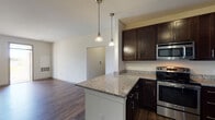 Located at 3 Woodview Way in Hopkinton, Massachusetts, this single-floor residence offers a well-designed layout with contemporary finishes throughout. The kitchen is a standout feature, outfitted with rich dark-stained cabinetry, granite countertops, a peninsula with pendant lighting, and a full suite of stainless steel appliances including a range, microwave, dishwasher, and refrigerator. The flooring throughout the main living areas and kitchen is a durable wood-style plank, adding warmth and continuity to the space. The open living area is bright and generously proportioned, with neutral walls, natural light from a large window, and a sliding glass door that leads to a private balcony with outdoor views — ideal for enjoying the surrounding New England landscape. The bedroom is carpeted for comfort and features a sizable window that frames views of the greenery outside, creating a calm and restful atmosphere. The bathroom is clean and functional, appointed with dark vanity cabinetry, a single-sink vanity with a mirror, and a full soaking tub with a tiled surround. The consistent use of dark cabinetry and wood-tone flooring gives the unit a cohesive, modern aesthetic throughout.