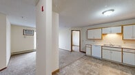 Located on Raven St NW in Coon Rapids, Minnesota, this two-bedroom, two-bathroom unit offers a functional single-floor layout designed for comfortable everyday living. The open-concept kitchen and living area form the heart of the space, with tile flooring in the kitchen transitioning to carpet in the living room. The kitchen features white cabinetry with wood-tone trim, ample counter space in an L-shaped configuration, a double sink, dishwasher, electric range, and a full-size refrigerator — providing everything needed for meal preparation. A textured ceiling runs throughout the main living areas, adding a classic residential touch. The living room is generously proportioned, anchored by a sliding glass door with vertical blinds that admits natural light and provides outdoor views. A wall-mounted air conditioning unit ensures year-round comfort. Both bedrooms are carpeted and well-sized, with the primary bedroom offering a window with neighborhood views and baseboard heating. The two bathrooms are each equipped with a tub-shower combination, toilet, and a vanity with ample cabinet storage beneath. Hallways connect the rooms efficiently, and a closet provides additional storage. The layout is straightforward and practical, making effective use of the available space throughout.