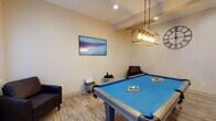 Located at 283 Cooper Pl in New Haven, Connecticut, this single-floor amenity space is designed to offer both recreation and wellness in a clean, modern setting. The layout is divided into two distinct areas: a game room and a fitness center, each thoughtfully appointed and finished to a contemporary standard.

The game room centers around a full-size pool table with a vibrant blue felt surface, set beneath a striking industrial-style pendant light fixture with exposed Edison bulbs. Light wood-look flooring runs throughout the room, contributing to a warm and inviting atmosphere. A wall-mounted flat-screen TV, a decorative oversized clock, and a wall-mounted cue rack complete the space, while comfortable seating provides a place to relax between games. Natural light filters in through white-shuttered windows, and an exterior door offers convenient access.

The adjacent fitness center features a well-rounded selection of exercise equipment, including a treadmill, stationary cycle, weight bench, dumbbell rack, and a multi-function cable machine. A smart fitness mirror adds a modern, interactive element to workouts. The room is finished with durable multi-tone carpet tiles, recessed ceiling lighting, and neutral gray walls, creating a focused and functional environment. Together, these two spaces provide a well-balanced amenity offering for residents.