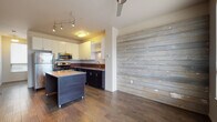 Located at 1618 Hazel Dr in Cleveland's 44106 zip code, this modern multi-floor residence spans three levels and blends contemporary design with rustic character. A defining feature throughout the home is the use of reclaimed wood accent walls — light-toned horizontal planks in the main living and kitchen areas, and rich dark vertical planks in the bedroom — adding warmth and visual interest to the otherwise clean, neutral interiors.

The kitchen is well-appointed with stainless steel appliances including a gas range, microwave, and refrigerator, complemented by dark lower cabinetry, white upper cabinets, a wood-toned backsplash, and a movable island with a light quartz surface. Rich hardwood flooring ties the kitchen and living areas together seamlessly.

The bedrooms feature plush carpeting and ceiling fans, with large windows that invite ample natural light and outdoor views. Closet space is thoughtfully designed with built-in shelving and sliding doors. The bathroom presents a clean, modern aesthetic with subway tile surrounding the tub and shower, large-format floor tiles, a vessel sink atop a wood-toned vanity, and brushed nickel fixtures.

The lower level includes an attached garage with automatic door opener, offering secure, convenient parking. The home's staircase connects all three floors cohesively, making this a functional and stylish residence.