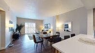 This thoughtfully designed single-floor residence offers a cohesive blend of modern finishes and comfortable living spaces. The open-concept layout seamlessly connects the living, dining, and kitchen areas, creating a spacious and functional flow throughout the home. Rich wood-tone flooring runs throughout, lending warmth and continuity to the space.

The living room is a standout area, anchored by plantation-shuttered sliding doors that flood the room with natural light and offer views of the surrounding cityscape. A textured white brick accent wall adds architectural character, complementing the neutral, contemporary palette.

The dining area accommodates a full-sized glass dining table and chairs, positioned between the kitchen and living room for easy entertaining. The kitchen is outfitted with stainless steel appliances, including a range, over-the-range microwave, and refrigerator, complemented by sleek wood-grain cabinetry and a vibrant teal subway tile backsplash set against crisp white countertops.

The bedroom is a serene retreat with soft neutral tones, offering a calm and restful ambiance. The bathroom features wood-grain tile flooring, a single-sink vanity with wood-tone cabinetry, a full shower-tub combo, and additional built-in storage — delivering both style and practicality in equal measure.