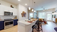 This thoughtfully designed single-floor residence offers a seamless blend of modern aesthetics and functional living. The open-concept kitchen is a standout feature, showcasing two-tone navy and white cabinetry, a classic subway tile backsplash, stainless steel appliances, and a spacious quartz waterfall island with bar seating illuminated by pendant lighting. The kitchen flows naturally into the bright living area, where light hardwood flooring, large windows, and a ceiling fan create an airy, welcoming atmosphere with generous natural light and outdoor views.

The bedrooms are carpeted for comfort, each offering a serene retreat. The primary bedroom benefits from wide windows that frame greenery outside, while a second bedroom provides equally cozy accommodations. The bathroom is elegantly finished with a double-sink vanity featuring navy cabinetry and quartz countertops, a soaking tub with dramatic dark tile surround, and a separate walk-in shower. A walk-in closet is conveniently accessible directly from the bathroom. The dedicated in-unit laundry room provides added practicality, housing a full-size washer and dryer. Consistent use of navy, white, and natural wood tones gives the entire space a cohesive, contemporary character.