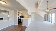 This two-story residence offers a thoughtfully designed layout that blends functionality with comfort. The main floor showcases an open-concept living and dining area distinguished by soaring vaulted ceilings and a ceiling fan, creating an airy, spacious feel. A white-mantled fireplace serves as the focal point of the living room, flanked by windows that invite natural light and views of the surrounding neighborhood. Sliding glass doors provide additional access to the exterior.

The kitchen is efficiently laid out in a galley style, featuring dark appliances including a black refrigerator and electric range, white cabinetry, and a light countertop surface. A peninsula counter connects the kitchen to the main living area, ideal for casual dining or entertaining. Rich wood-toned flooring runs throughout the kitchen and entry areas, while plush carpet covers the living and bedroom spaces.

Upstairs, the bedrooms are generously proportioned with vaulted or angled ceiling lines, carpeted floors, and natural light from recessed windows. The primary suite includes a walk-in closet with built-in shelving and a vanity area with a marble-look countertop and mirror. Additional bedrooms offer closet space and share access to the upper level. The overall palette of soft neutrals throughout lends the home a clean, move-in-ready appearance.
