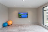 Located at 117 Fitchburg Dr in Woodstock, GA, this single-floor fitness and wellness facility is thoughtfully designed to support a range of exercise activities. The space is defined by light hardwood-style flooring throughout, recessed ceiling lighting, and a neutral warm-gray color palette that creates a clean, modern atmosphere.

A standout architectural feature is the floor-to-ceiling glass partition wall with sleek dark-framed sliding doors, which separates a dedicated equipment gym area from the open exercise floor. The enclosed gym houses cardio machines, a cable system, a weight bench, and a dumbbell rack, all visible through the transparent glass wall. Full-length mirrors within the gym section further enhance the sense of depth and openness.

The open exercise area provides ample space for stretching, yoga, or floor-based workouts, and includes a wall-mounted large-format television for interactive or media-guided sessions. Large windows and a sliding glass door offer direct views of a resort-style outdoor pool and surrounding community, filling the space with natural light and an energizing outdoor connection. Multiple electrical outlets and panel controls are positioned conveniently along the walls throughout the space.