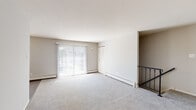 Located at 275 E High St in Glassboro, New Jersey, this single-floor unit offers a clean, functional layout designed for comfortable everyday living. The open living area features neutral-toned carpet throughout, light gray walls, and ample space for a variety of furniture arrangements. Large vertical blinds and sliding glass door access fill the room with natural light, while baseboard heating ensures year-round comfort. A wrought iron staircase railing adds a subtle decorative touch near the entry level transition.

The kitchen stands out with rich, dark wood cabinetry, white countertops, and a full suite of stainless steel appliances including a gas range, over-the-range microwave, and refrigerator. The tile flooring and clean lines give the kitchen a modern, polished feel.

The bedrooms are generously proportioned, each with soft carpeting and natural light from multiple windows fitted with blinds. One bedroom features dual louvered closet doors, providing notable storage capacity. The bathroom is neatly appointed with tile flooring, a tub-shower combination with white tile surround accented by a navy tile border, and a window for natural ventilation. Throughout the unit, the neutral color palette and practical finishes create a bright, move-in-ready environment.