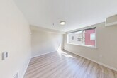 Located at 1221 NE 180th St in Shoreline, WA, this one-bedroom, one-bathroom unit offers a thoughtfully designed single-floor layout with modern finishes throughout. Light-toned luxury vinyl plank flooring runs through the main living areas, complemented by clean white walls and recessed lighting that create a bright, cohesive aesthetic.

The kitchen is a standout feature, equipped with dark wood-grain cabinetry extending to the ceiling for ample storage, white countertops, and a full suite of black appliances including a range, microwave, dishwasher, and French door refrigerator. A sliding barn door adds a contemporary architectural touch connecting the kitchen corridor to the rest of the unit.

The living area receives natural light through a large window with views of the surrounding neighborhood. The bedroom is a comfortable, well-proportioned space with direct access to a spacious walk-in closet outfitted with wire shelving systems and soft carpet underfoot.

The bathroom features wood-toned cabinetry, a vanity sink, and clean tile-style flooring, maintaining the unit's modern design language. An additional unclassified room with carpeted flooring provides flexible utility space. The long, well-lit hallway with louvered closet doors ties the layout together, offering a clean and functional flow throughout.