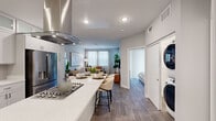 This well-designed one-bedroom, one-bathroom residence offers a thoughtfully organized single-floor layout that maximizes every square foot. The open-concept kitchen is a standout feature, showcasing floor-to-ceiling white shaker cabinetry with frosted glass upper panels, quartz countertops, a large center island with bar seating, a stainless steel range hood, gas cooktop, and a full suite of stainless steel appliances including a refrigerator, dishwasher, microwave, and oven. Wood-look plank flooring flows seamlessly throughout the main living areas, lending warmth and continuity to the space. The living room is bright and inviting, with multiple windows that draw in natural light, and offers comfortable space for both relaxing and entertaining. The bedroom is a calm retreat featuring a ceiling fan, a walk-in closet with a sliding barn door, and sliding glass doors dressed with vertical blinds that allow for adjustable light control. The bathroom is clean and modern, featuring quartz countertops, white cabinetry, tile flooring, and a full soaking tub with shower. A stacked washer and dryer unit is conveniently located within the residence. The overall ambiance is contemporary and bright, with a neutral color palette that creates a calm, cohesive atmosphere throughout.
