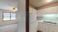 Located at 118 Broadhurst Rd in Jacksonville, NC, this single-story home offers a straightforward and functional layout across a well-organized floor plan. The kitchen is equipped with ample white cabinetry providing generous storage, light countertops, a double-basin sink, a built-in cooktop, and wood-look flooring that adds warmth to the space. An under-cabinet light fixture illuminates the work area, while the U-shaped design maximizes efficiency. Adjacent to the kitchen, the living area features carpet flooring and a ceiling fan with integrated lighting, along with a window that allows natural light to brighten the room. Throughout the home, the bedrooms are carpeted and feature textured ceilings, neutral-toned walls, and windows with blinds that provide natural light and privacy. One bedroom includes a built-in closet with dark wood-toned doors, adding a touch of contrast to the lighter walls. The panel-style wall accents found in select rooms contribute a subtle architectural detail to the interior. The overall layout, as seen in the dollhouse view, presents a compact yet well-connected arrangement of rooms, making this a practical and accessible single-level residence.