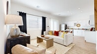 This single-floor residence offers a thoughtfully designed open-concept layout that seamlessly connects the living, dining, and kitchen areas. The living room is a welcoming space bathed in natural light from large windows dressed with blackout curtains, showcasing warm wood-look flooring, crisp white walls, and a cozy seating arrangement centered around a solid wood coffee table. A stylish credenza and curated wall art add character to the room.

The kitchen is well-equipped with a full suite of stainless steel appliances, including a refrigerator, dishwasher, microwave, and range. White shaker cabinetry provides ample storage, complemented by neutral stone-tone countertops and a functional layout that makes meal preparation effortless. A dining area adjacent to the kitchen comfortably accommodates a round table with seating.

The bedroom is a serene retreat featuring wood-look flooring, soft natural light from a curtained window, and a spacious walk-in closet with built-in shelving and hanging rods. Two bathrooms serve the residence — each finished with white vanity cabinetry, stone-tone countertops, undermount sinks, and chrome fixtures. One bathroom features a shower-tub combination, while the other includes a glass-enclosed walk-in shower with white tile surround.