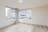 This contemporary single-floor unit offers a clean, modern aesthetic defined by light wood-style flooring, neutral warm-white walls, and an abundance of natural light. The open living area is anchored by expansive floor-to-ceiling windows that frame sweeping urban views of the surrounding cityscape, bringing a strong sense of connection to the vibrant environment outside.

The kitchen is thoughtfully designed with rich warm-toned wood cabinetry featuring built-in wine storage, white countertops, a stainless steel sink, and a full suite of stainless steel appliances including a dishwasher, range, and built-in microwave. Track lighting overhead provides excellent task illumination throughout the space.

Multiple bedrooms are present, each featuring large windows with city views, light flooring, and ceiling fans in select rooms for added comfort. The layout is efficiently organized, with a hallway connecting the private areas to the main living spaces. Recessed lighting in the corridor adds a polished architectural touch.

The bathroom is finished in a clean, minimal style with a warm wood vanity, white countertop, chrome fixtures, and a full soaking tub with shower. A second full tub-shower combination is also present. The overall ambiance is bright, airy, and move-in ready, suited for urban living.