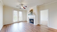 This single-floor residence offers a thoughtfully designed layout with a clean, neutral palette throughout. The living room serves as the heart of the home, showcasing warm hardwood-style flooring, crown molding, a ceiling fan, and a classic white-mantled fireplace that anchors the space. French doors flood the room with natural light and provide access to the outdoors. The kitchen is well-equipped with rich cherry wood cabinetry, granite countertops, stainless steel appliances including an electric range and built-in microwave, and a stylish subway tile backsplash. A built-in desk area with matching cabinetry and open shelving offers a dedicated workspace or study nook. The primary bathroom features granite countertops, cherry wood vanity, a glass-enclosed walk-in shower, hardwood-style flooring, and direct access to a spacious walk-in closet complete with wire shelving. A second full bathroom mirrors the same granite and cabinetry finishes, with a tub-shower combination and ample vanity mirror. Bedrooms are carpeted for comfort, with ceiling fans and generous natural light from blinds-covered windows. A large walk-in closet with wire rack shelving adds to the home's practical storage solutions throughout.
